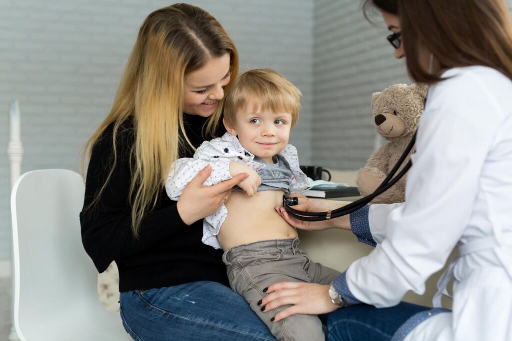 Medic pediatru care examinează un copil în cabinet, în prezența mamei