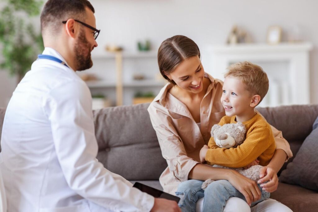 Medic consultând un copil mic zâmbitor, aflat în brațele tatălui, într-un cabinet de medicină de familie