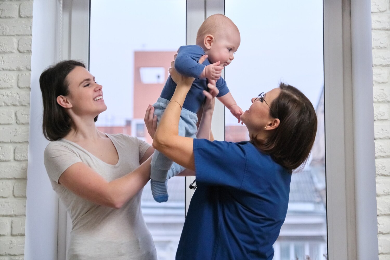 Medic de familie discutând cu o mamă despre vaccinarea copiilor, în timp ce aceasta își ține bebelușul în brațe